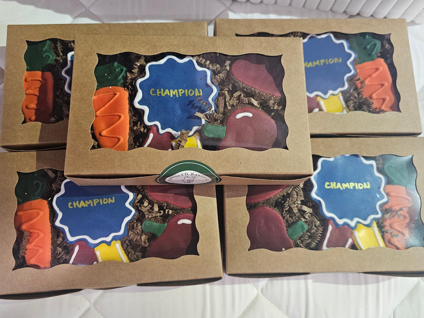 Three cardboard boxes containing colorful horse cookies labeled 'Champion' on a white quilted surface.