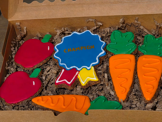 A set of decorated apple flax horse including two red apples with green tops, two orange carrots with green tops and a blue ribbon cookie with the word 'CHAMPION' 